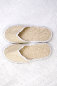 Top view of eco-friendly hotel guest slippers made from breathable woven material placed on a white towel.