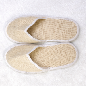Top view of eco-friendly hotel guest slippers made from breathable woven material placed on a white towel.